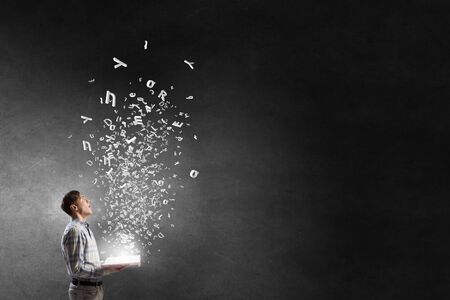 Close view of man with opened book in hands and characters flying in airの写真素材