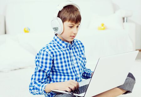 Boy of school age listening music from laptop through headphones while sitting on floor