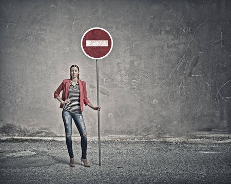 Young lady in red jacket standing and holding stop signの写真素材