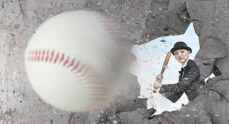 Young woman in suit and cylinder hitting ball with baseball bat