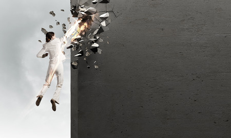 Emotional businesswoman breaking stone wall with karate punchの写真素材