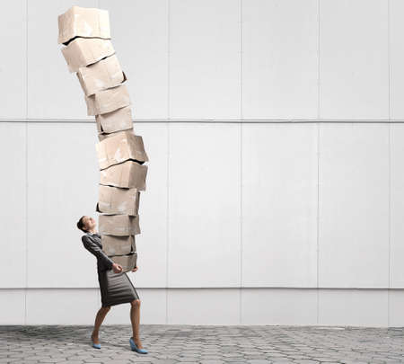 Attractive businesswoman carrying big stack of carton boxes