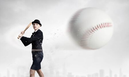 Young woman in suit and cylinder hitting ball with baseball batの写真素材