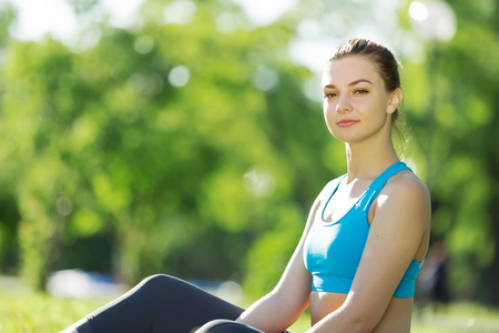 Beautiful sport girl sitting on grass in park and relaxingの写真素材