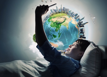 Teenager boy in bed using his tablet pc for entertainment. Elements of this image are furnished by NASAの写真素材