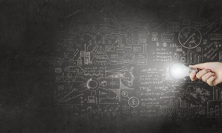 Glowing light bulb in person hand throwing light on business sketchesの写真素材