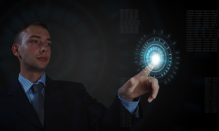 Young businessman on dark background touching icon of media screenの写真素材