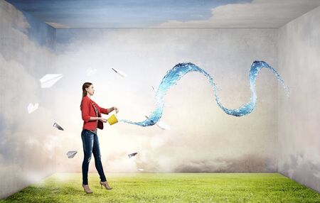 Young woman pouring water from yellow bucketの写真素材