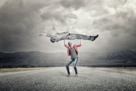 Young woman in red jacket lifting man above headの写真素材
