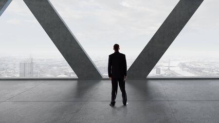 Back view of businessman in modern room looking in office windowの写真素材