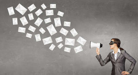 Unrecognizable businesswoman hiding her face behind mask and screaming in megaphoneの写真素材