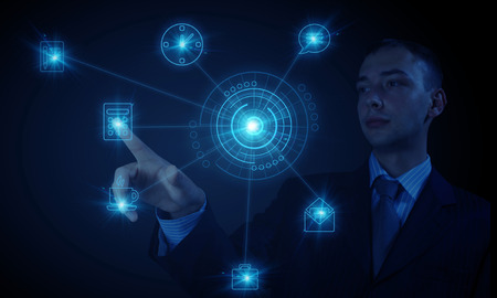 Young businessman on dark background touching icon of media screenの写真素材