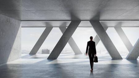 Businesswoman with suitcase in modern interior looking in office windowの写真素材