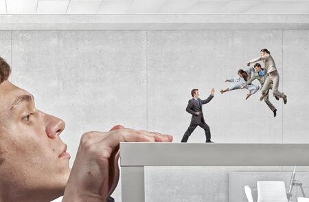 Young businessman looking from under table on fighting peopleの写真素材
