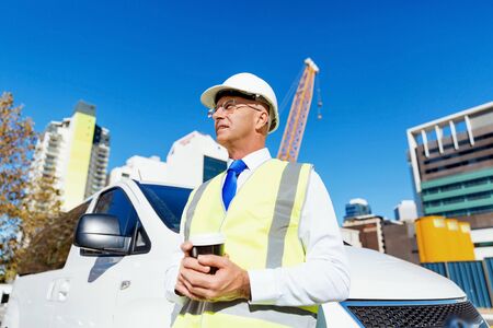 Engineer builder wearing safety vest with coffee at construction site
