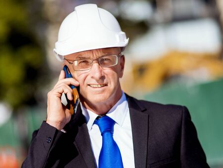 Businesman wearing safety helmet with mobile phone at construction site