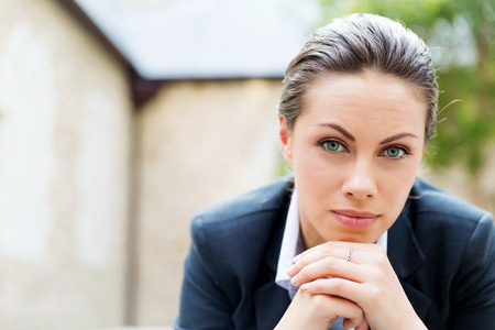 Portrait of young business woman outdoors sitting and thinkingの写真素材
