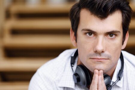 Portrait of young businessman sitting at the stairs in office with headphonesの写真素材
