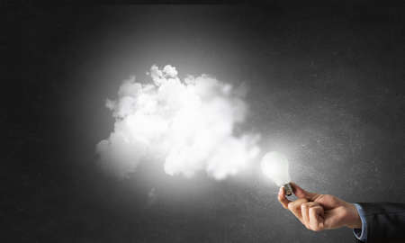 Glowing light bulb in person hand throwing light on darknessの写真素材