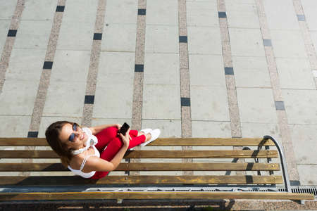 Attractive girl using smart phone and texting sitting on bench of parkの写真素材