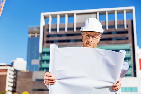Engineer builder wearing safety vest with blueprint at construction siteの写真素材