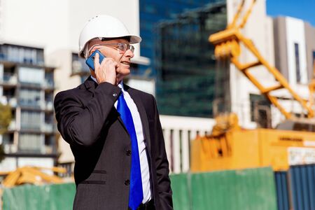 Businesman wearing safety helmet with mobile phone at construction site