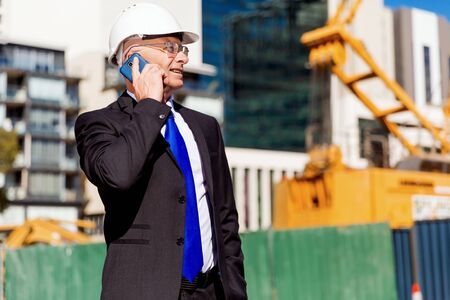 Businesman wearing safety helmet with mobile phone at construction siteの写真素材