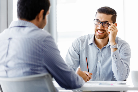 Two handsome businessman in office sitting at desk and talkingの写真素材