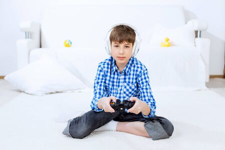 Emotional kid boy sitting on floor playing games on joystick