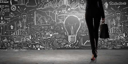 Rear view of businesswoman with suitcase looking at business ideas on wallの写真素材