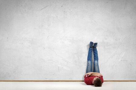 Young man lying on floor with legs raised up on wallの写真素材