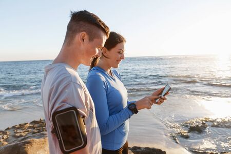 Two young people in sport wear with smartphones outdoors