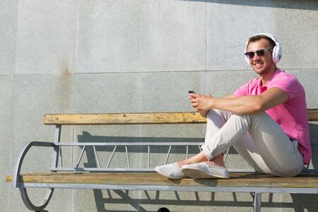 Happy guy on wooden bench listening to music from his smartphoneの写真素材