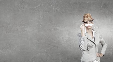 Attractive businesswoman in hat trying on paper mustacheの写真素材