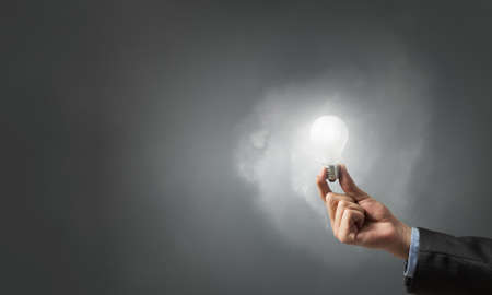 Glowing light bulb in person hand throwing light on darknessの写真素材