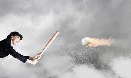 Young woman in suit and cylinder hitting ball with baseball batの写真素材