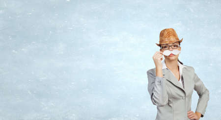 Attractive businesswoman attaching paper mustache to her faceの写真素材