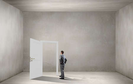 Young businessman in concrete room and opened door with no way outの写真素材