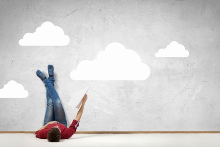 Young man lying on floor with legs raised up on wallの写真素材