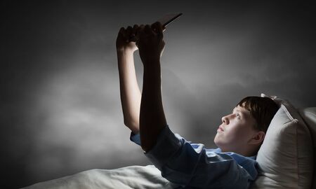 Teenager boy in bed using his tablet pc for entertainmentの写真素材