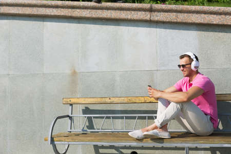 Happy guy on wooden bench listening to music from his smartphoneの写真素材