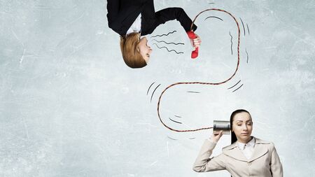 Young pretty businesswoman attaching tin phone to earの写真素材