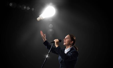 Young businesswoman speaking in microphone on dark backgroundの写真素材