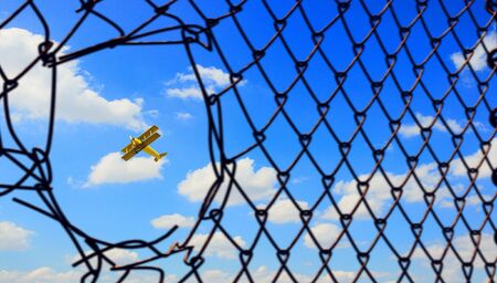 Old airplane seen in fence hole flying in clear blue sky