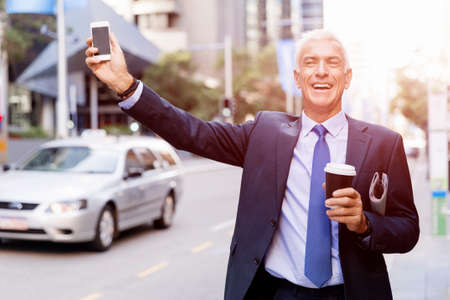 Businessman in suit catching taxi in city with cup of coffee in his handsの写真素材
