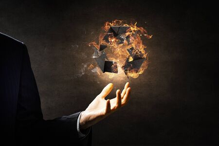 Recycle sign in fire flames in palm on dark background