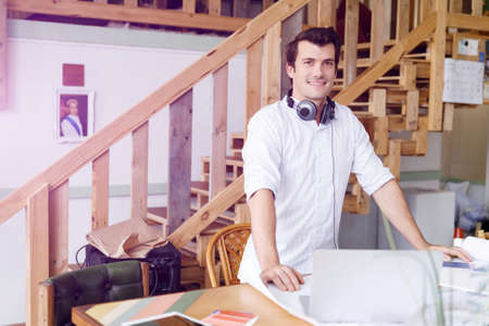 Smiling young designer standing in creative office in front of his desk
