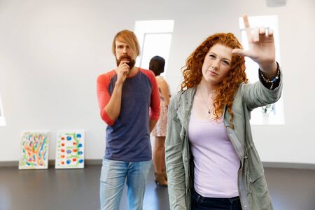 Young artists in gallery hanging together painting on wallsの写真素材