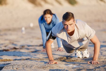 Young couple of man and woman doing push ups on ocean beach
