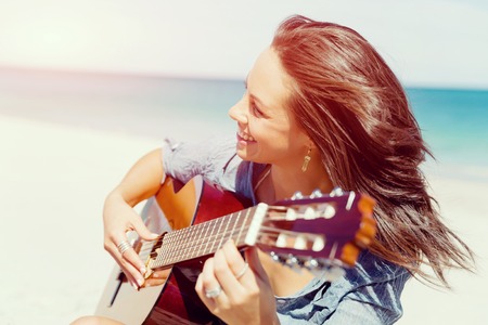 Beautiful young smiling woman playing guitar on beachの写真素材